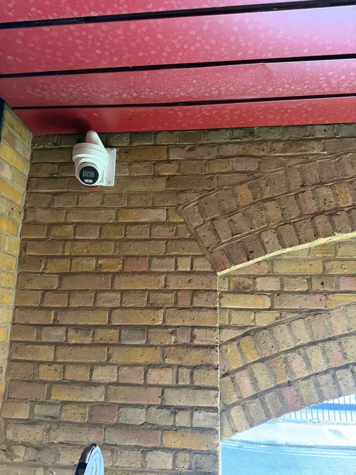 Turret CCTV camera installed on a brick wall beneath a red canopy