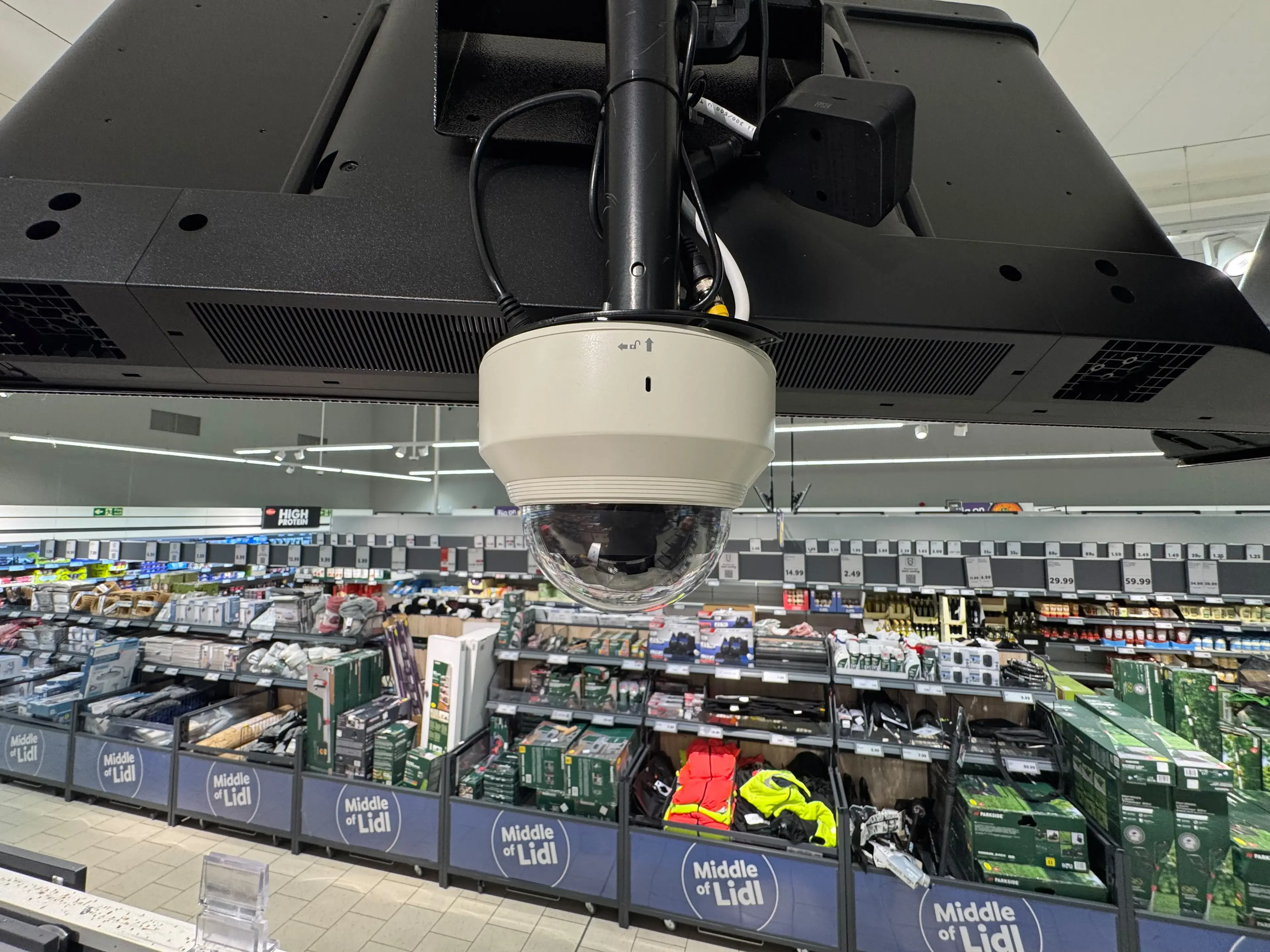 Dome camera mounted beneath a supermarket ceiling monitor