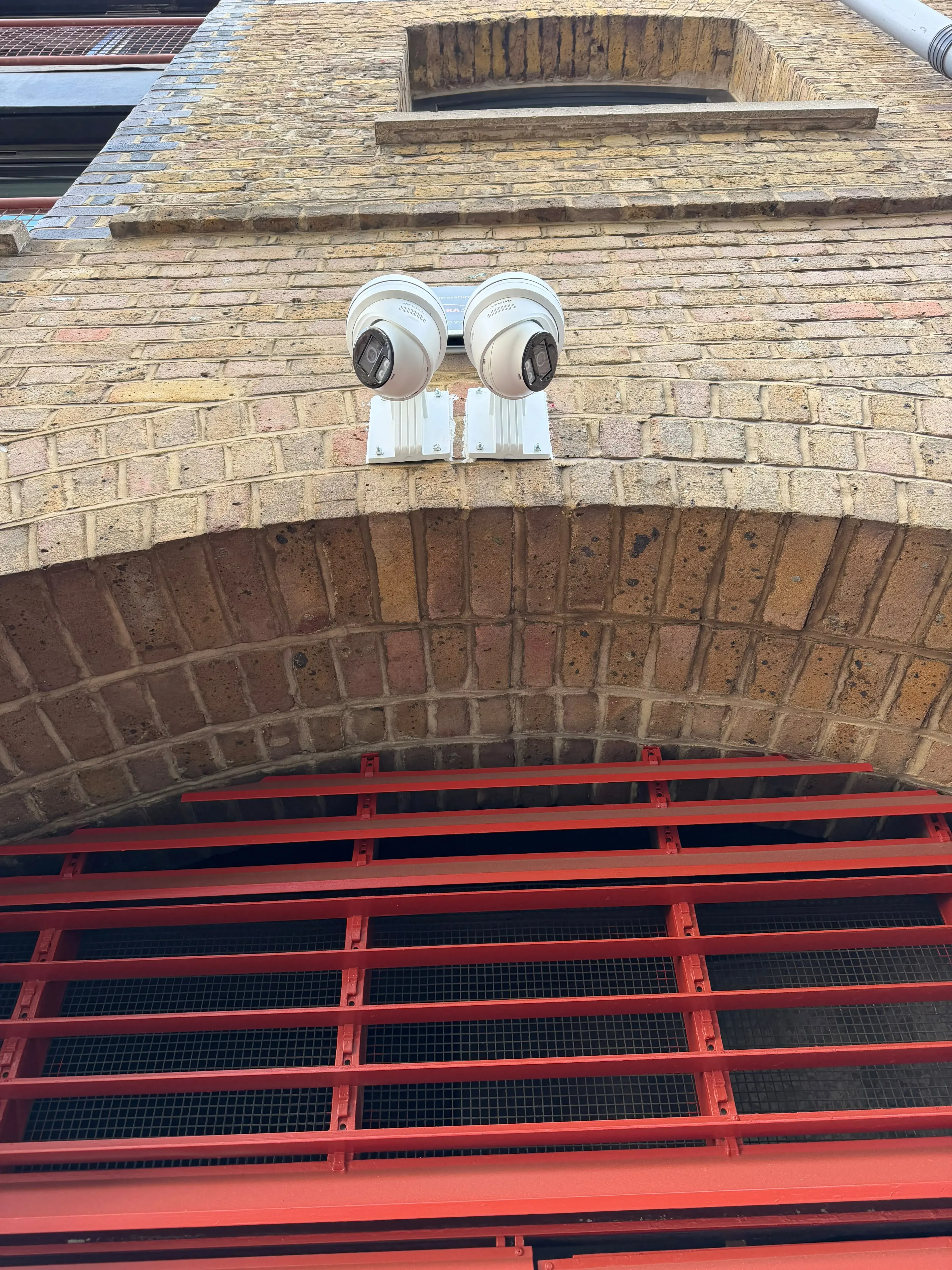 Two turret CCTV cameras mounted above a brick archway